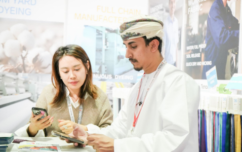 Three men in white shirts talking and examining products at a trade show booth